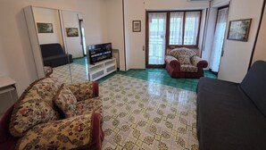 A living room with a sofa, a chair, a TV on a stand, and a patterned floor. - Stephen's Tourist Accommodation (Lido di Ostia)