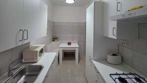 A modern kitchen with white cabinets, a stainless steel sink, a small table, and a gas stove. - Stephen's Tourist Accommodation (Lido di Ostia)