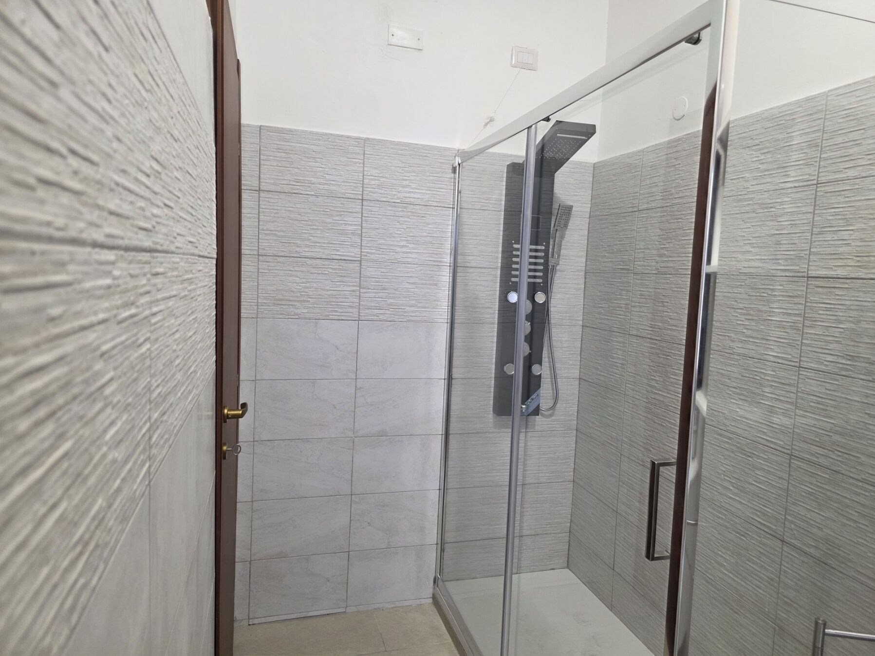 A modern bathroom with a glass shower enclosure, tiled walls, and a visible showerhead.