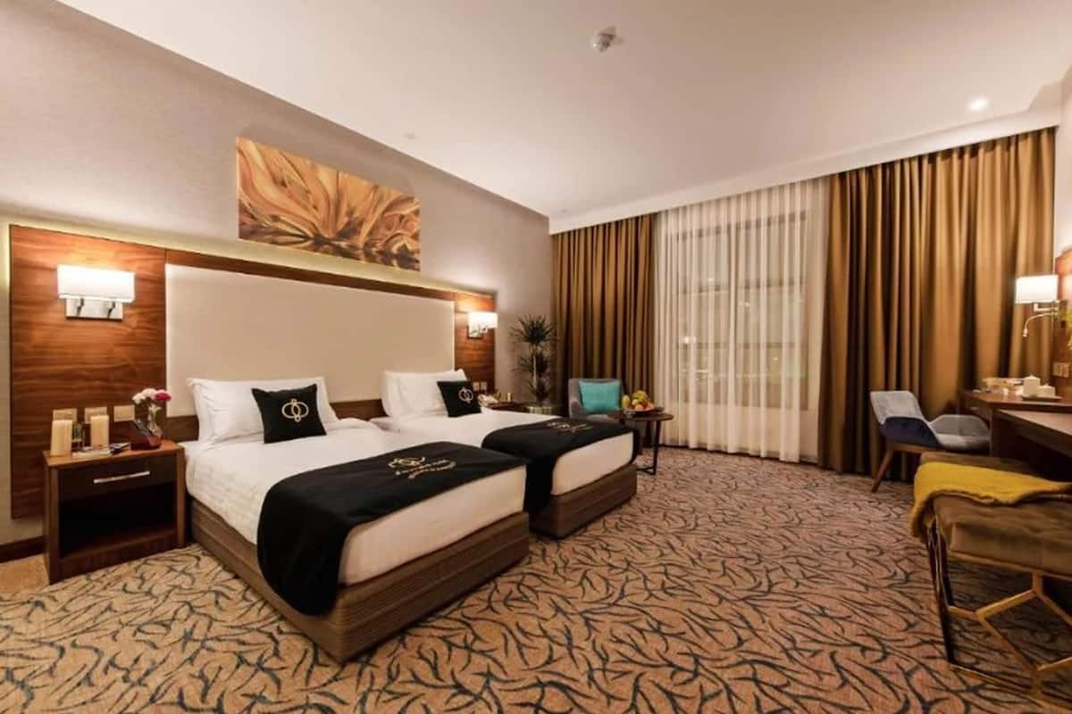 Habitación de hotel con dos camas, una obra de arte grande en la pared, un escritorio con silla y vistas al exterior a través de amplias ventanas.