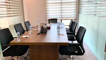 Un salón de conferencias con una larga mesa, sillas negras, botellas de agua, un teléfono y un jarrón.