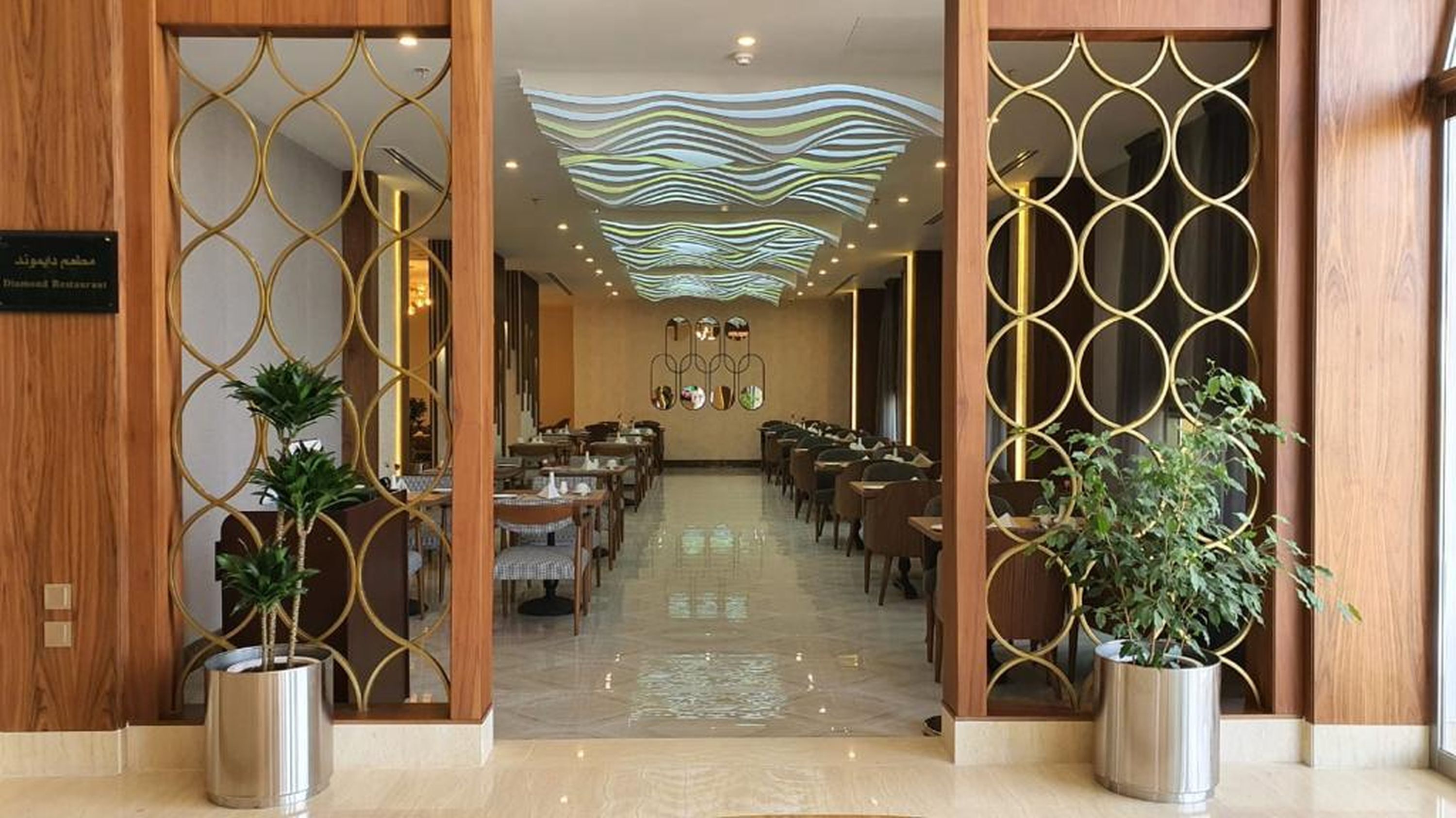 A spacious hotel lobby with a modern ceiling design, a central seating area, and potted plants.
