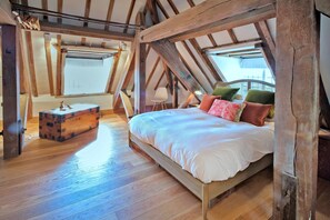 A bedroom with a wooden ceiling, a bed with pillows, a suitcase, and a small table. - The Loft at Brackley Town Hall (Brackley)