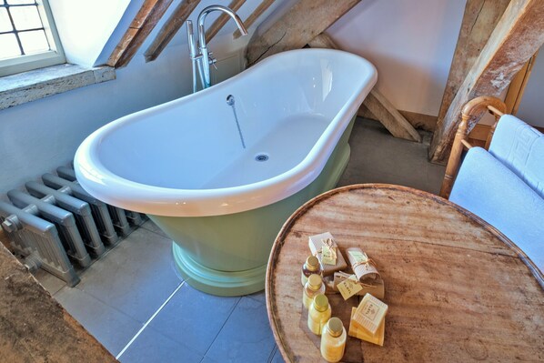 A bathroom with a freestanding bathtub, a wooden table with toiletries, and a window with a view of the outside. - The Loft at Brackley Town Hall (Brackley)