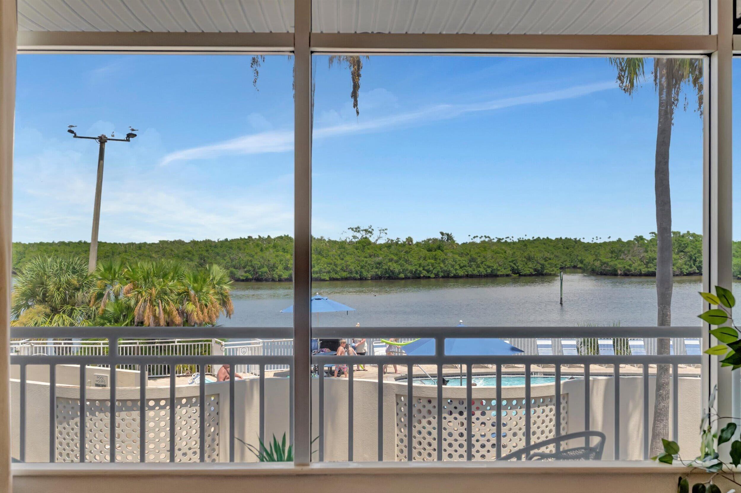 Un balcón con vista a un lago, palmeras y una zona de piscina.