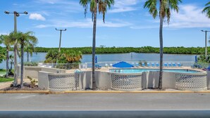 A pool area with palm trees, a view of a lake, and a fenced pool deck.