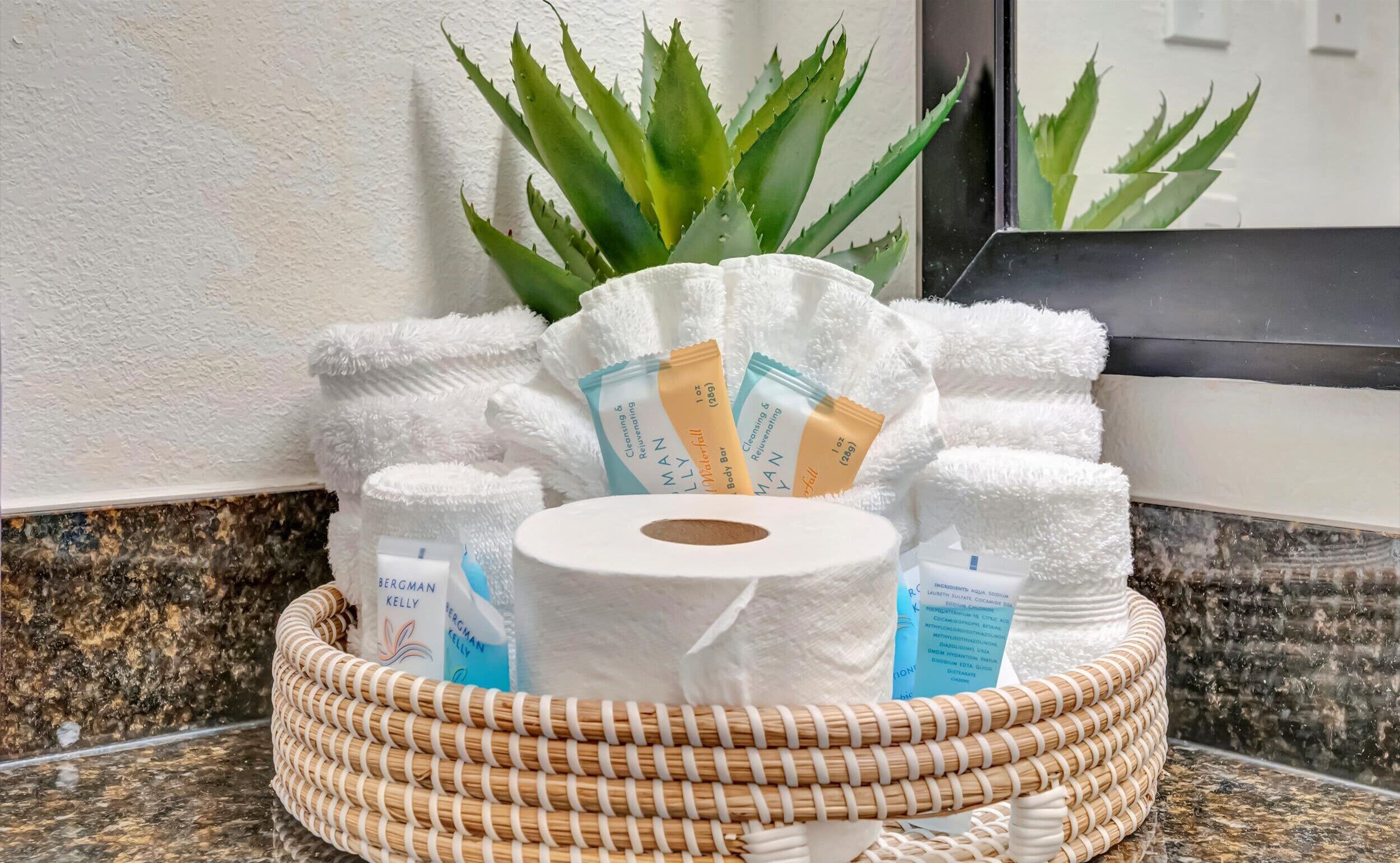 Un mueble de baño con una cesta tejida que contiene artículos de aseo, un espejo y una planta de aloe vera.
