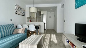 Ett modernt vardagsrum med en soffa, ett soffbord, en tv och en matplats med stolar och ett bord.