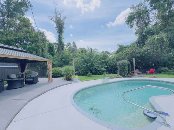 A backyard with a swimming pool, a covered patio with furniture, and a wooden structure. - Beautiful Villa with a private pool (Little River)