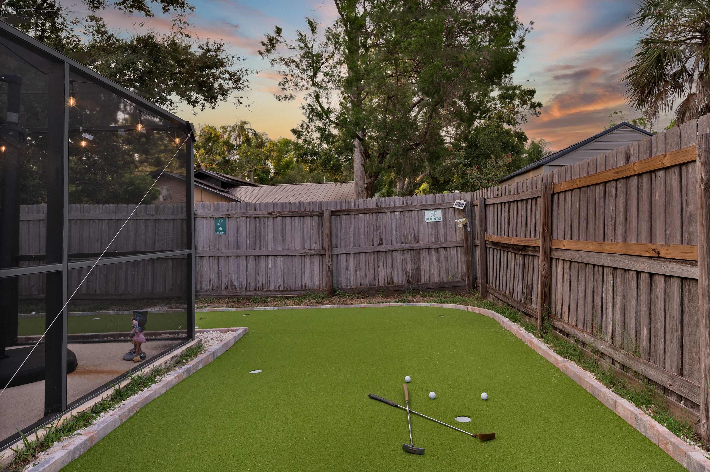 A backyard with a putting green, a wooden fence, and a glass structure.