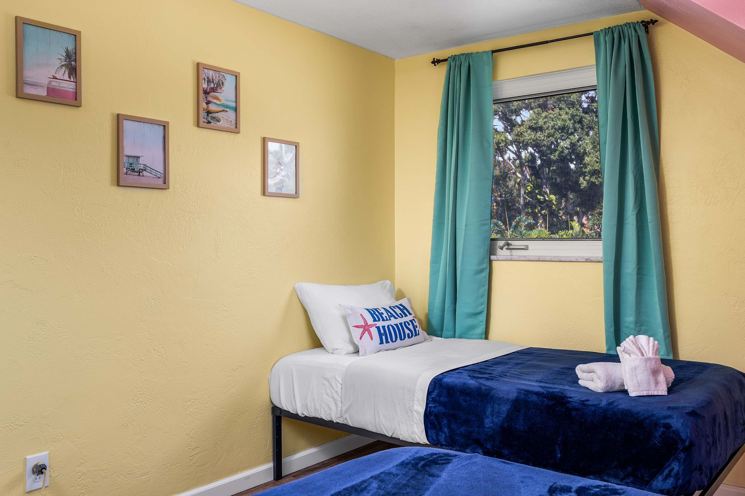 A room with a bed, a window with green curtains, and three framed pictures on the wall.