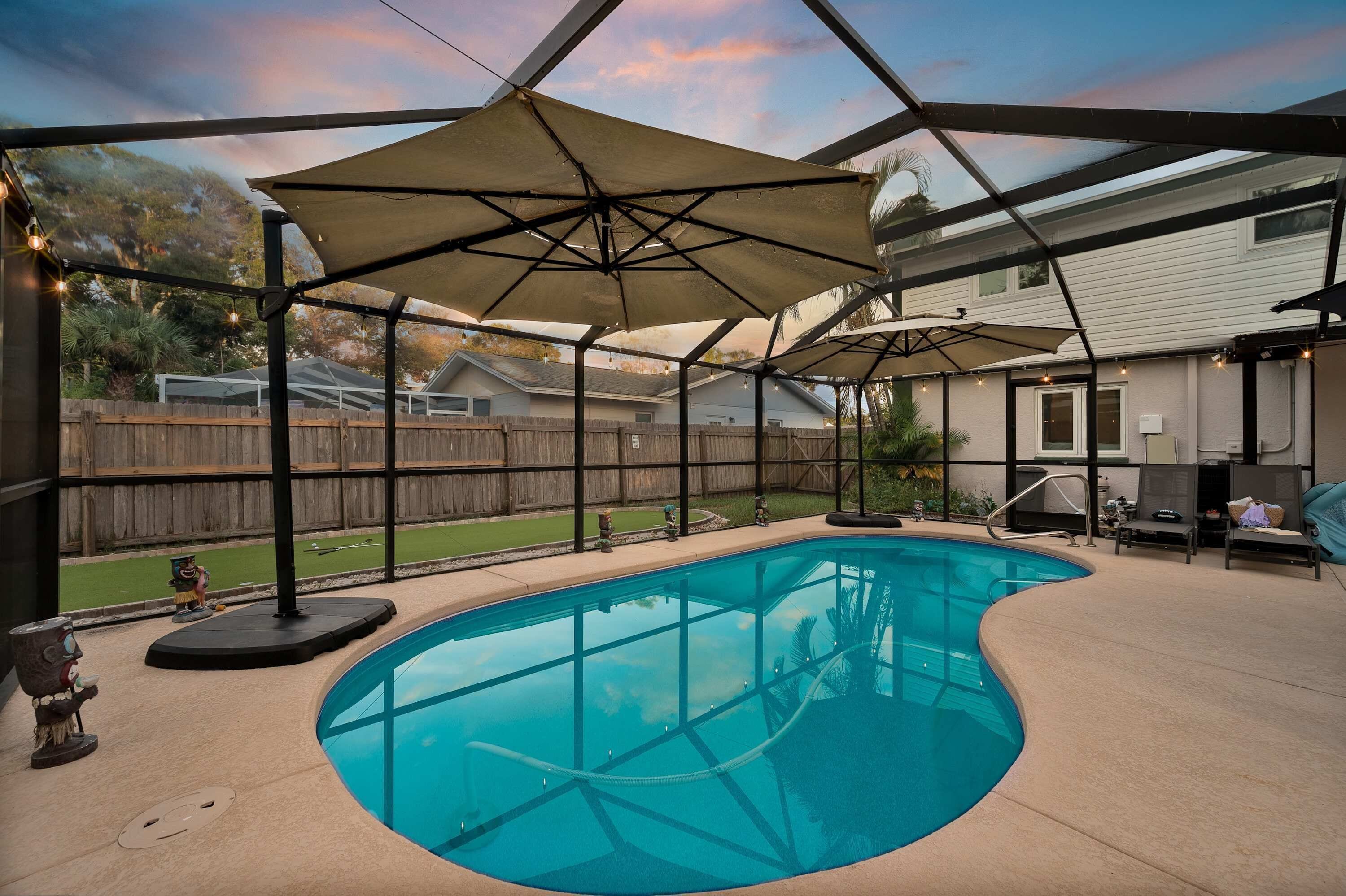 A backyard with a swimming pool, covered patio area, and outdoor furniture.