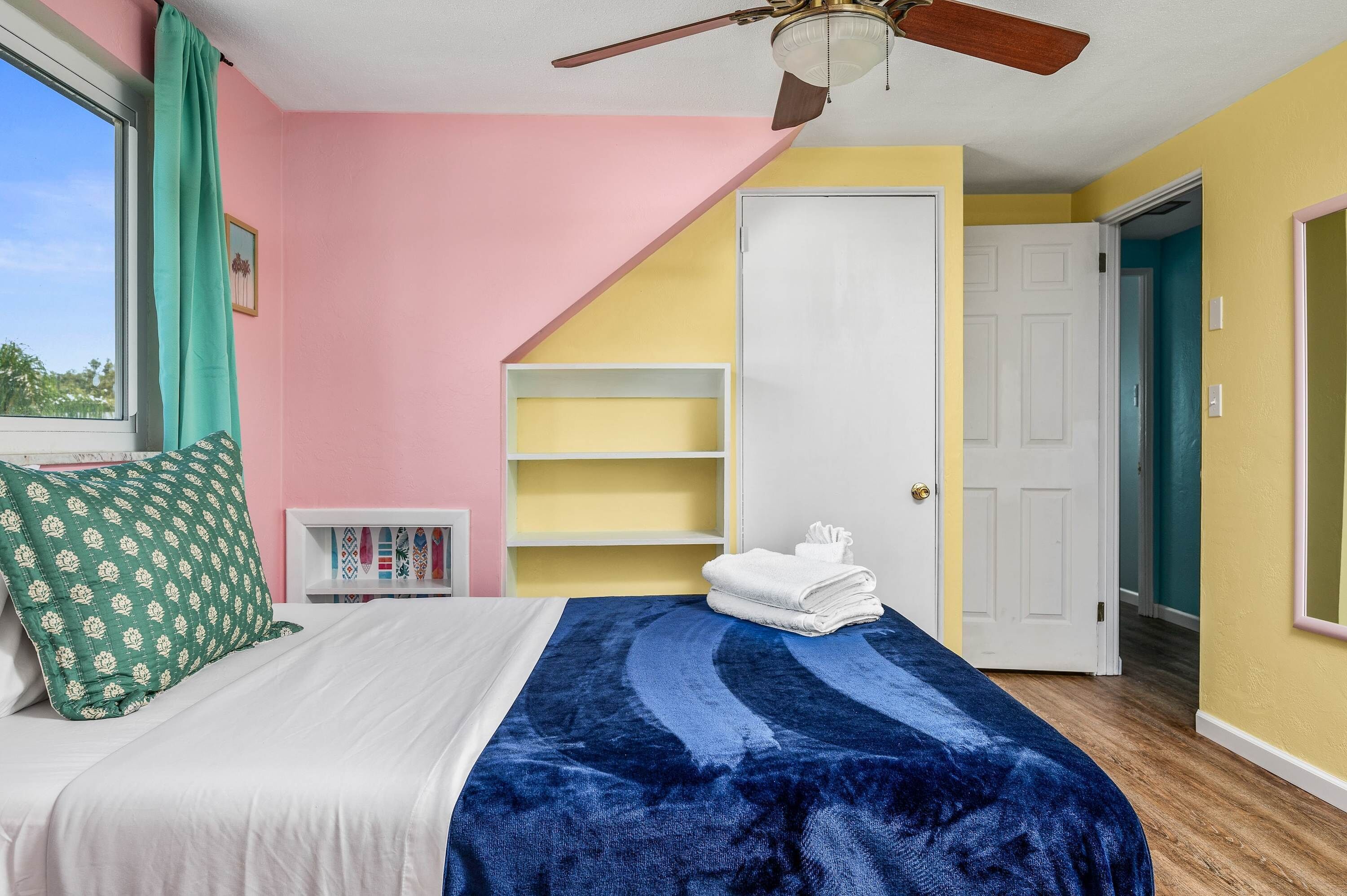 Une chambre à coucher avec un lit, un ventilateur de plafond, une fenêtre avec des rideaux et une porte.