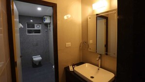 A bathroom with a toilet, a sink, a mirror, and a shower. - LGP Residency (Tiruchirappalli)