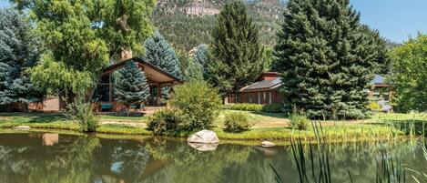 A lodge with a wooden cabin, a pond, and a mountain backdrop.