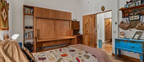 A bedroom with a bed, wooden wardrobe, shelves, and a blue dresser.