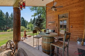 A wooden cabin with a patio area featuring a round wooden table, two chairs, a wooden bench, and a rustic lantern. - Single Level, Monthly Rental, Pond out Back! (Durango)