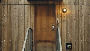 A wooden door with a metal handle and a keypad lock, a small light fixture above it, and a metal stairway leading up to the door.