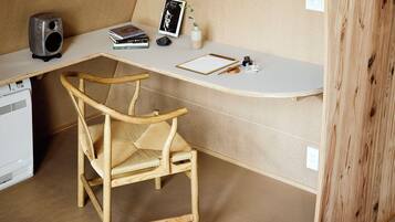 A workspace with a white desk, a wicker chair, a speaker, a framed photo, a book, and a small vase with a plant.