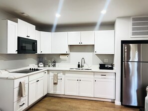 A modern kitchen with white cabinets, a stainless steel refrigerator, a built-in oven, and a microwave.
