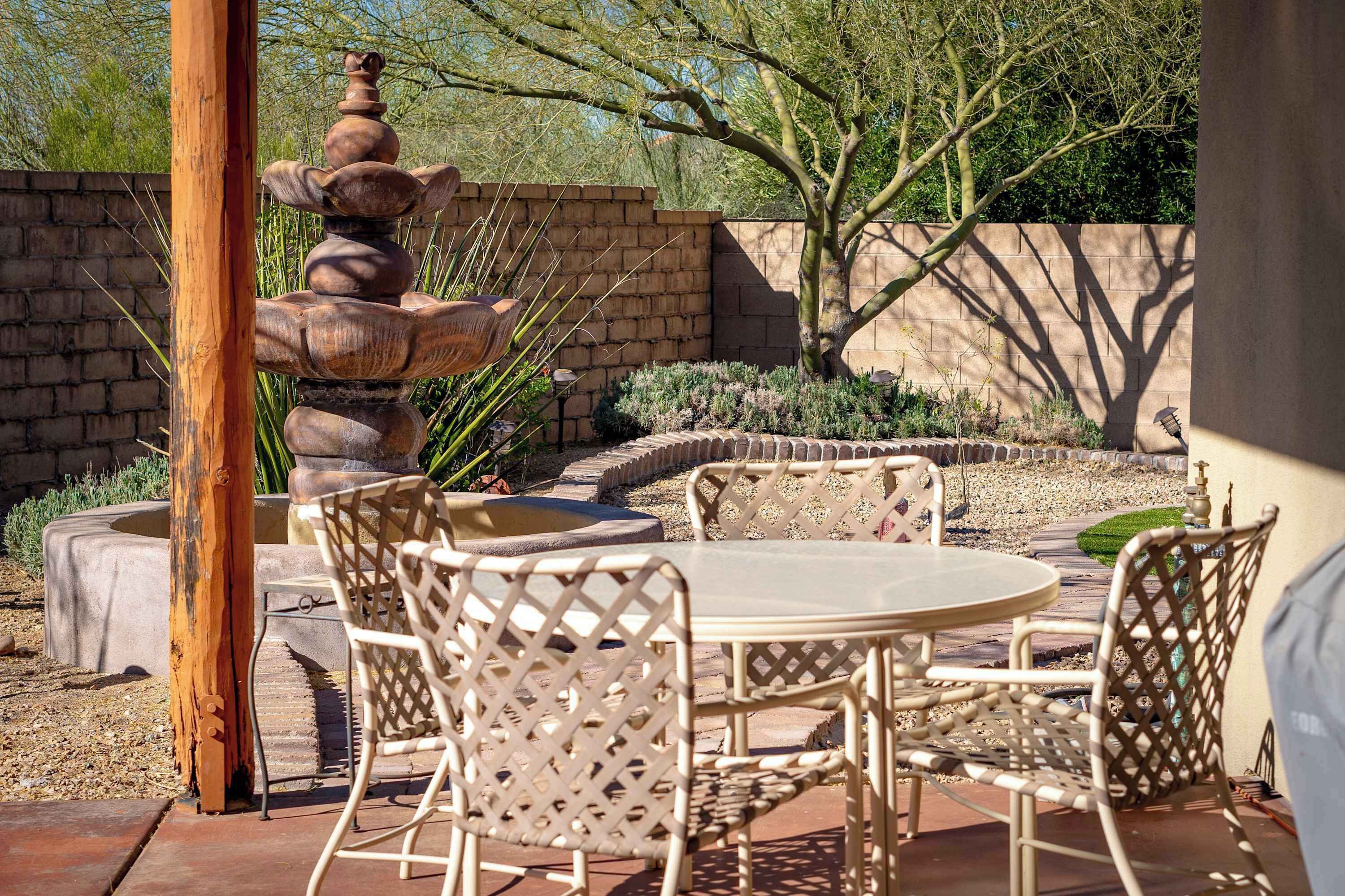 Eine Terrasse mit rundem Tisch und Stühlen, einer Steinfountain und einer Ziegelwand.