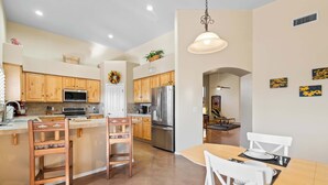 Una cocina moderna con armarios de madera, electrodomésticos de acero inoxidable y una zona de comedor con sillas blancas y una mesa de madera.