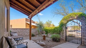 Un patio con zona de estar cubierta, pared de piedra y entrada con reja.