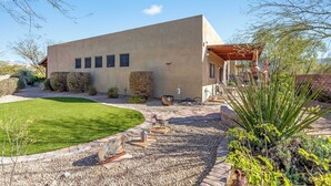 Una casa moderna con techo plano, un patio con pérgola y un césped bien cuidado.