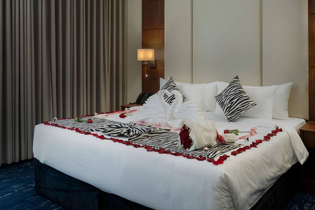 Een keurig opgemaakt bed met witte lakens, rode rozenblaadjes en een kussen met een zebraprint.