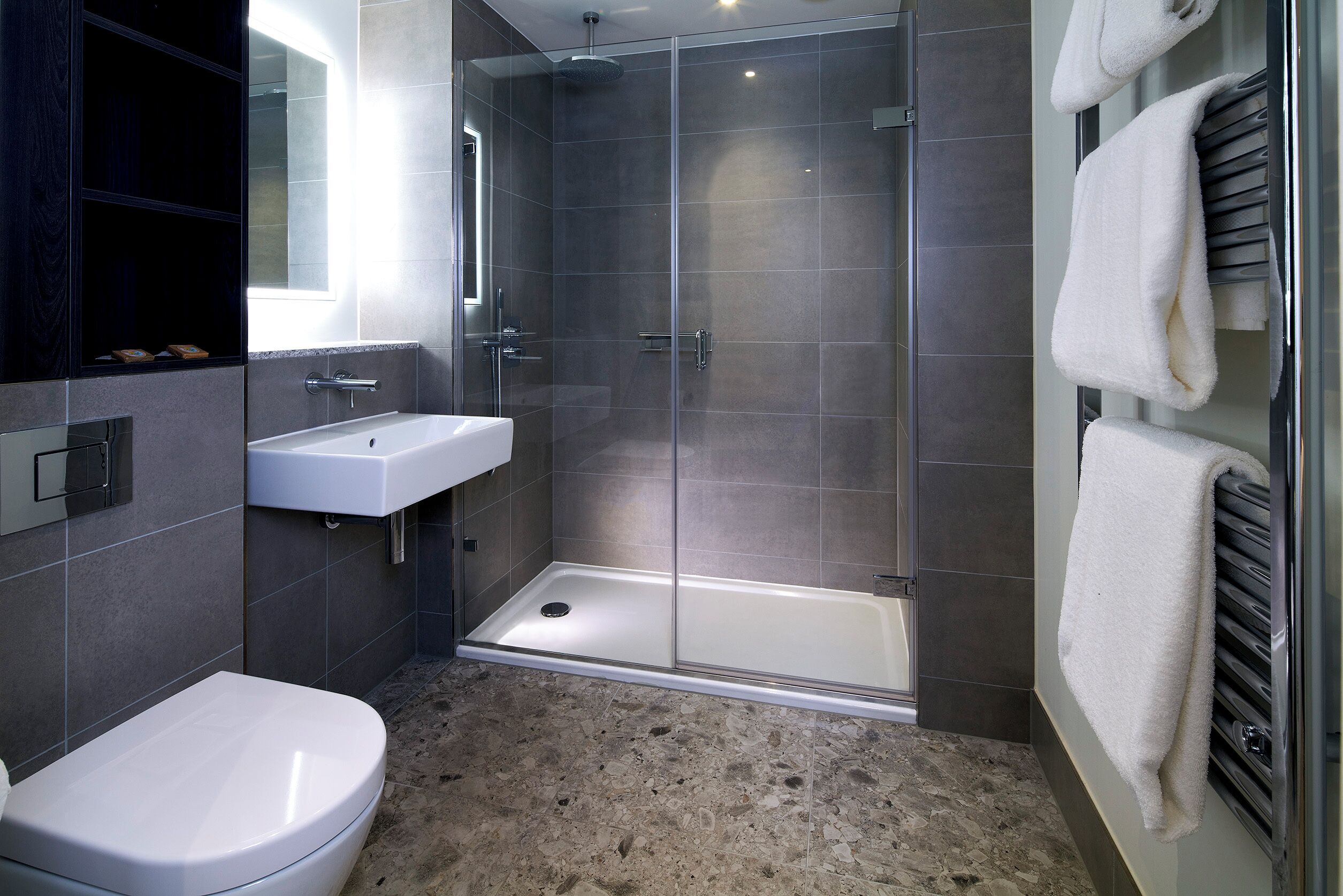 Un baño moderno con ducha envuelta en vidrio, lavamanos blanco y un inodoro.