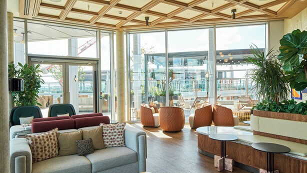 Ein stilvoller Lounge-Bereich mit einer Couch, Sesseln und einem Couchtisch. Große Fenster bieten Blick auf die Stadtlandschaft.