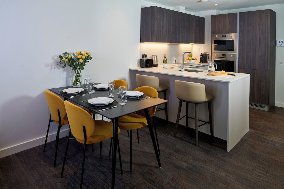 Une cuisine moderne avec des meubles en bois foncé, un îlot central et un coin repas doté de chaises jaunes.