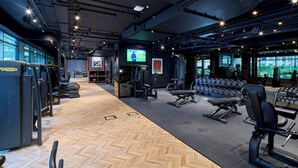 Ein Fitnessraum mit Trainingsgeräten, einem Fernseher und Blick ins Freie.