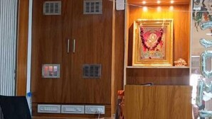 A reception desk with a wooden finish, a ceiling fan, and a wall-mounted display case with a framed item. - Shera Inn (Ahmedabad)