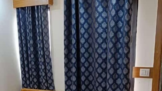 A bedroom with a bed, a wooden bench, and a patterned curtain. - Shera Inn (Ahmedabad)