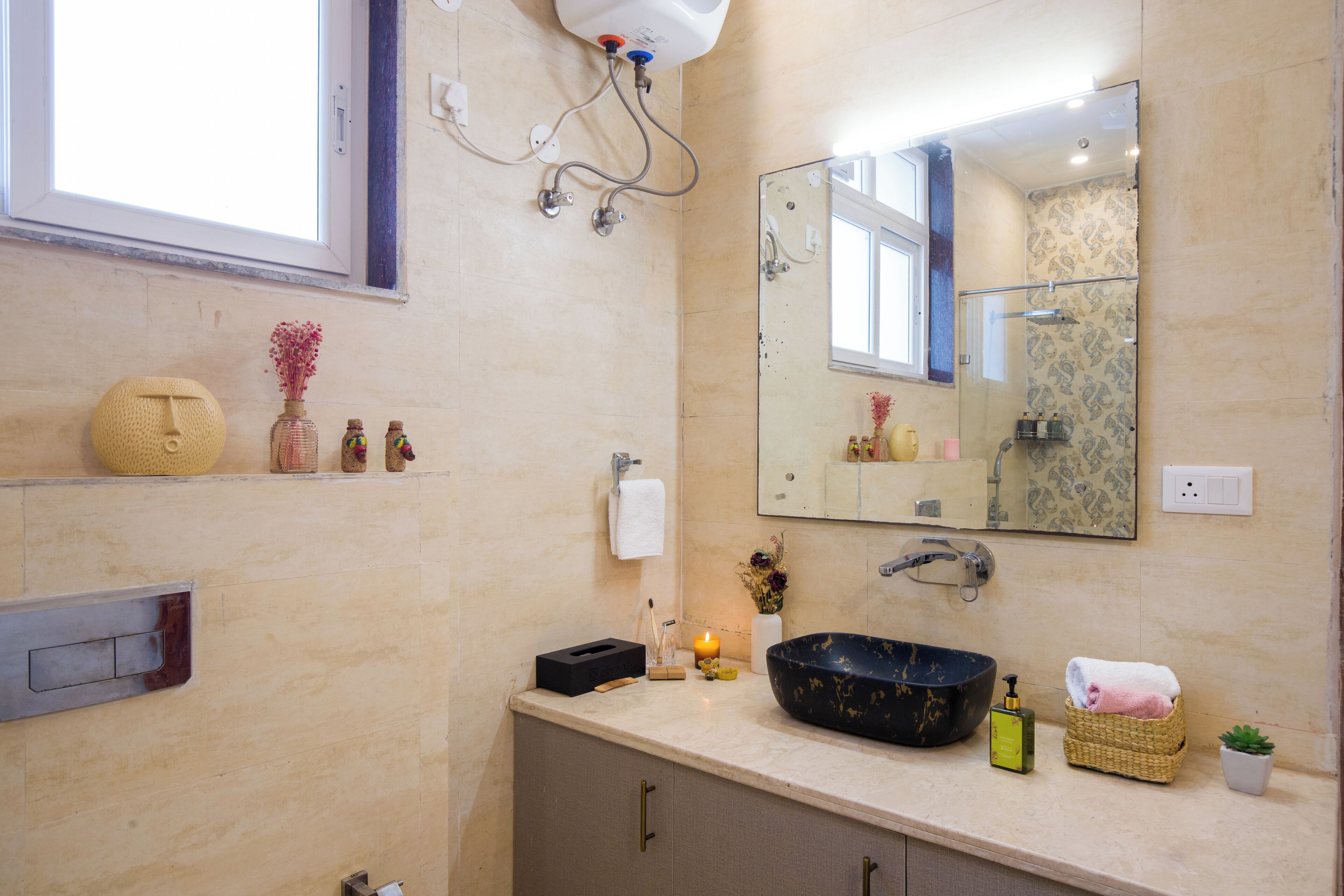 Une salle de bain avec un grand miroir, un lavabo et une douche. On y trouve des étagères avec des articles de toilette et une petite plante.