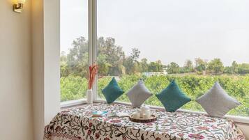 A room with a large window, a bed with a floral bedspread, and a view of greenery outside.