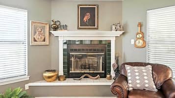 A room with a fireplace, a framed portrait, a guitar, and a leather armchair.