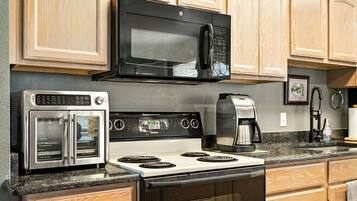 Una cocina con un microondas negro, un horno de acero inoxidable y una cafetera.