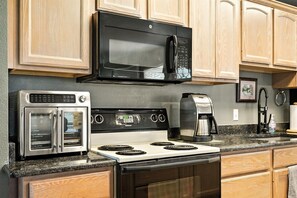 A kitchen with a black microwave, a stainless steel oven, and a coffee maker.