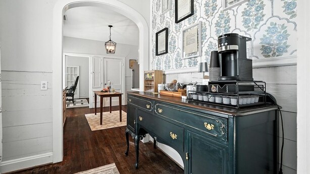 A kitchen with a vintage coffee machine, a wooden cabinet with brass handles, and a patterned wallpaper. - Big House on Highland: Your Country Escape (Abilene)