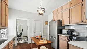 A kitchen with wooden cabinets, a refrigerator, a microwave, and a dining table with a placemat. - Big House on Highland: Your Country Escape (Abilene)