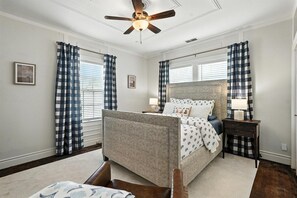 A bedroom with a bed, a nightstand, a ceiling fan, and checkered curtains. - Big House on Highland: Your Country Escape (Abilene)