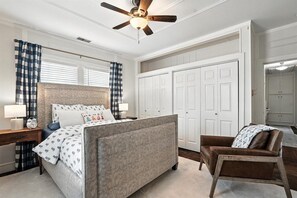 A bedroom with a bed, a chair, a desk, a wardrobe, and a ceiling fan.
