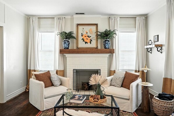 A living room with a fireplace, two sofas, a coffee table, and decorative plants.