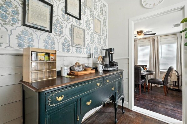 A room with a dark wooden cabinet, framed certificates on the wall, and a dining area with a table and chairs.