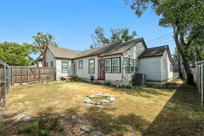A single-story house with a front yard, a stone fire pit, and a wooden fence.