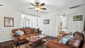 A living room with a brown leather sofa, a wooden coffee table, and a ceiling fan. - Big House on Highland: Your Country Escape (Abilene)
