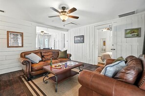 A living room with a brown leather sofa, a wooden coffee table, and a ceiling fan.