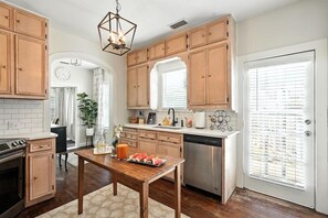A kitchen with wooden cabinets, a stainless steel dishwasher, and a dining table with a fruit plate. - Big House on Highland: Your Country Escape (Abilene)